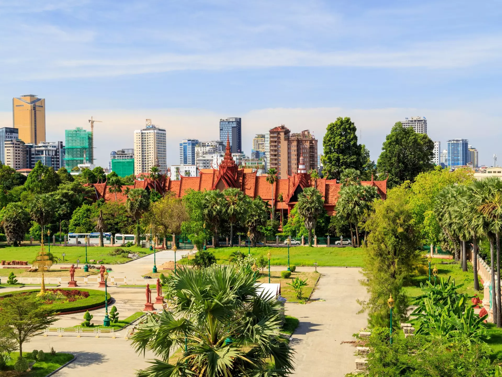 A park in the foreground leads to a building, only visible at its angled red roofline; a city skyline forms the horizon.