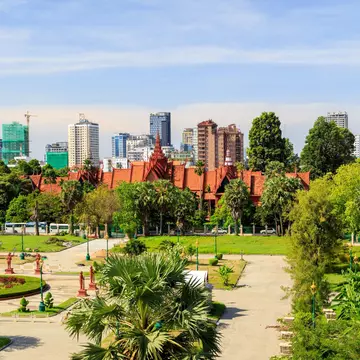 A park in the foreground leads to a building, only visible at its angled red roofline; a city skyline forms the horizon.