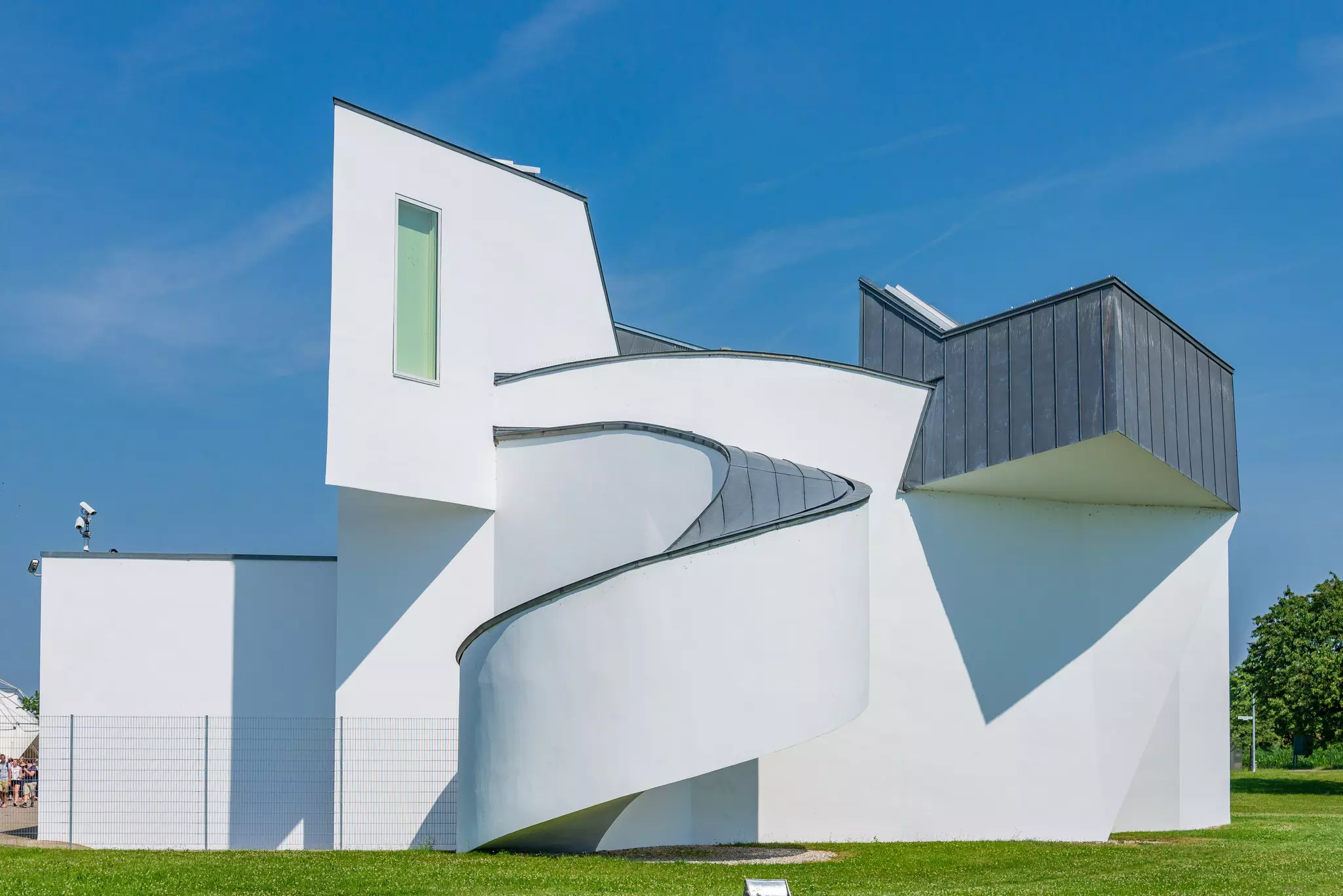 A modern white building has a curved ramp and tower with windows