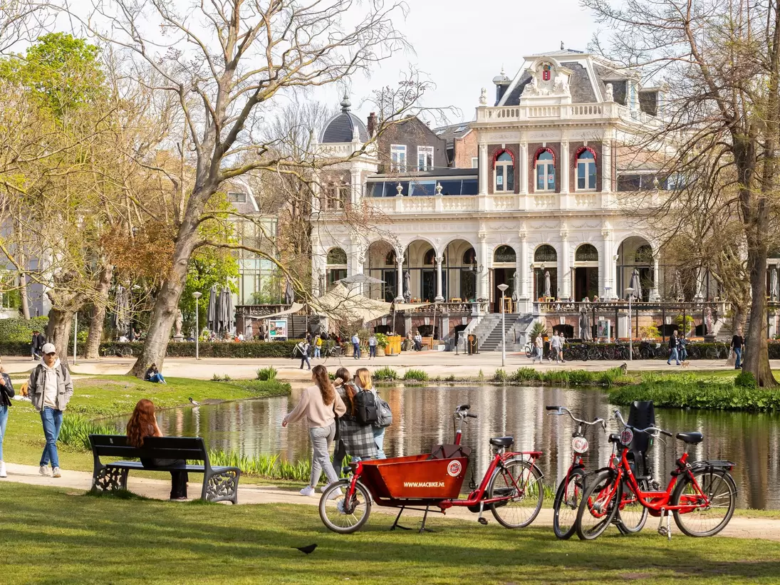 Tourists walk and cycle in the famous Vondelpark with the Vondelpark Pavilion in the background, Amsterdam.