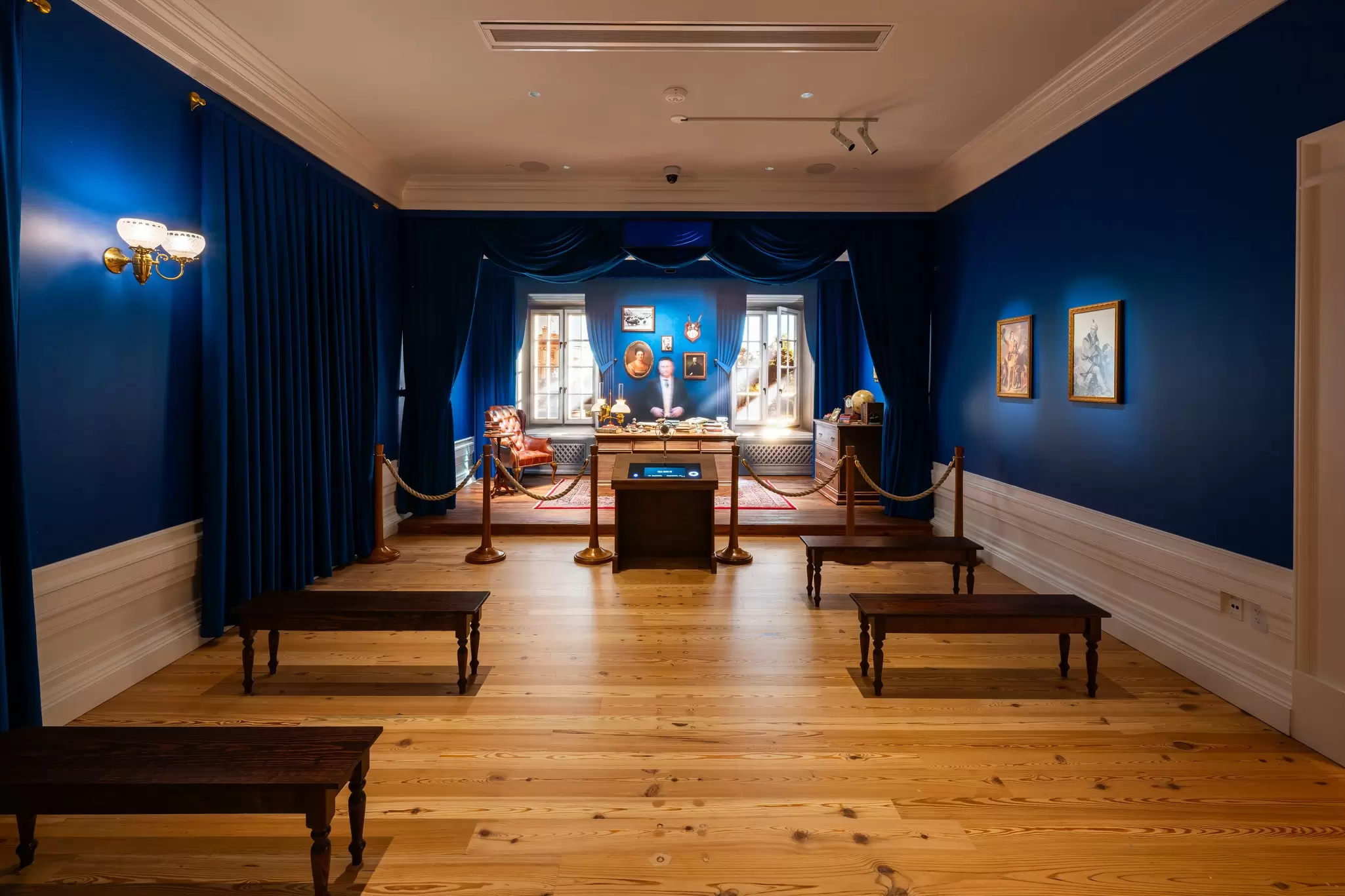 A room with blue walls, a desk, a chair and some benches for visitors to enjoy the Talk with TR Gallery.