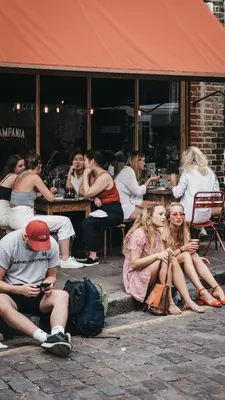 People sitting on the ground on Erza Street, relaxing after visiting Columbia Road Flower Market, a street market in East London that is open every Sunday.