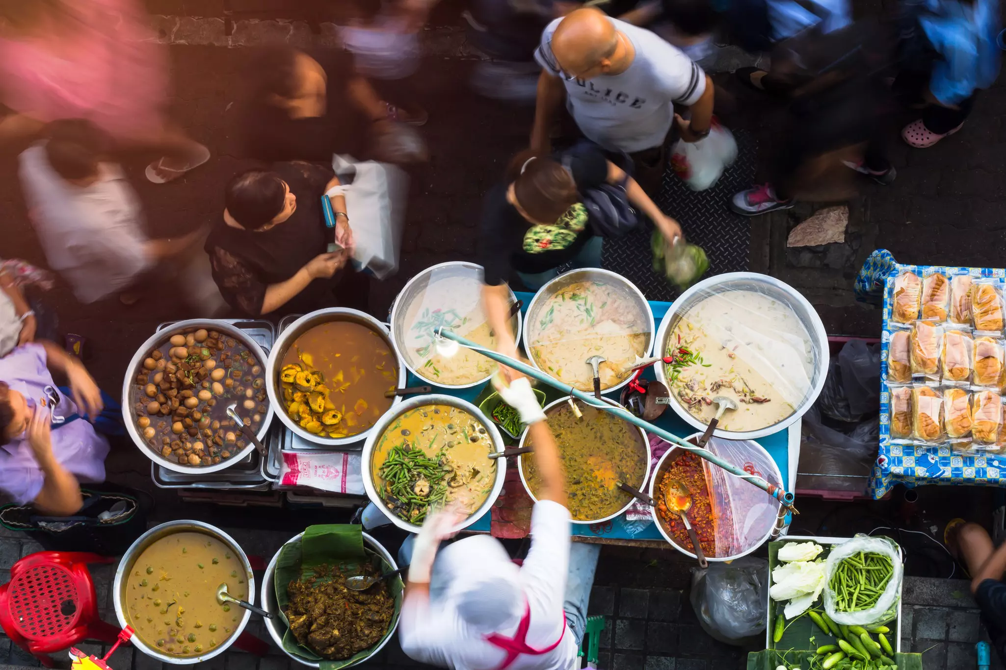 An overhead shot of a food stall crowded with large pots at a busy market
