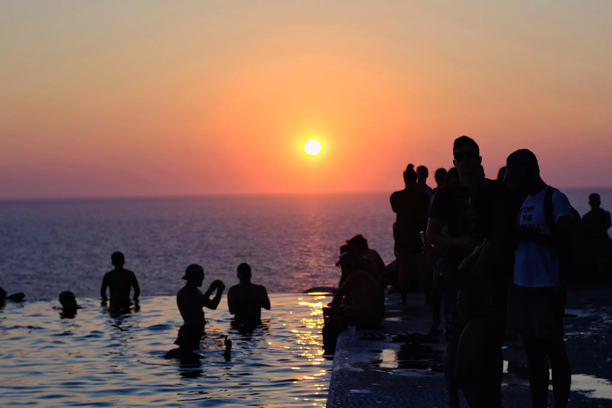 People in a pool in the Cyclades, Greece, watch the sunset.