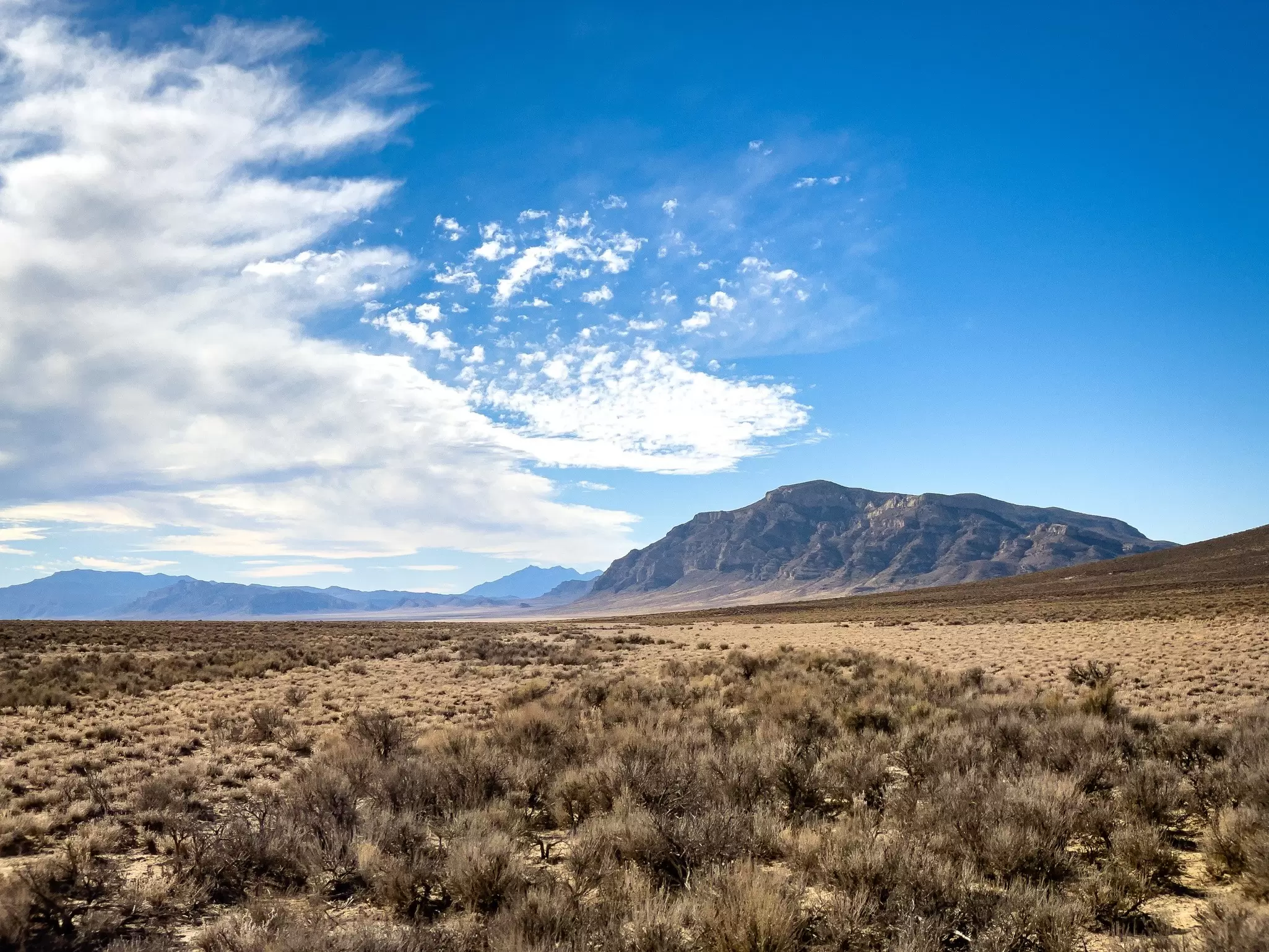 Sagebrush plain stretching to a distant flat-topped mountain under a blue sky with wispy white clouds