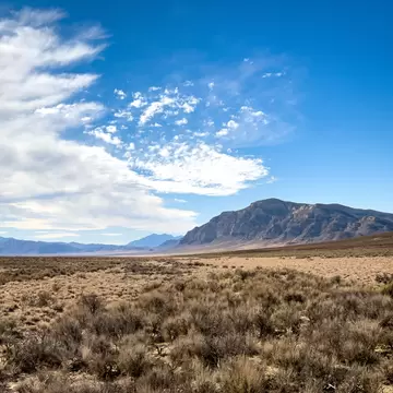Sagebrush plain stretching to a distant flat-topped mountain under a blue sky with wispy white clouds
