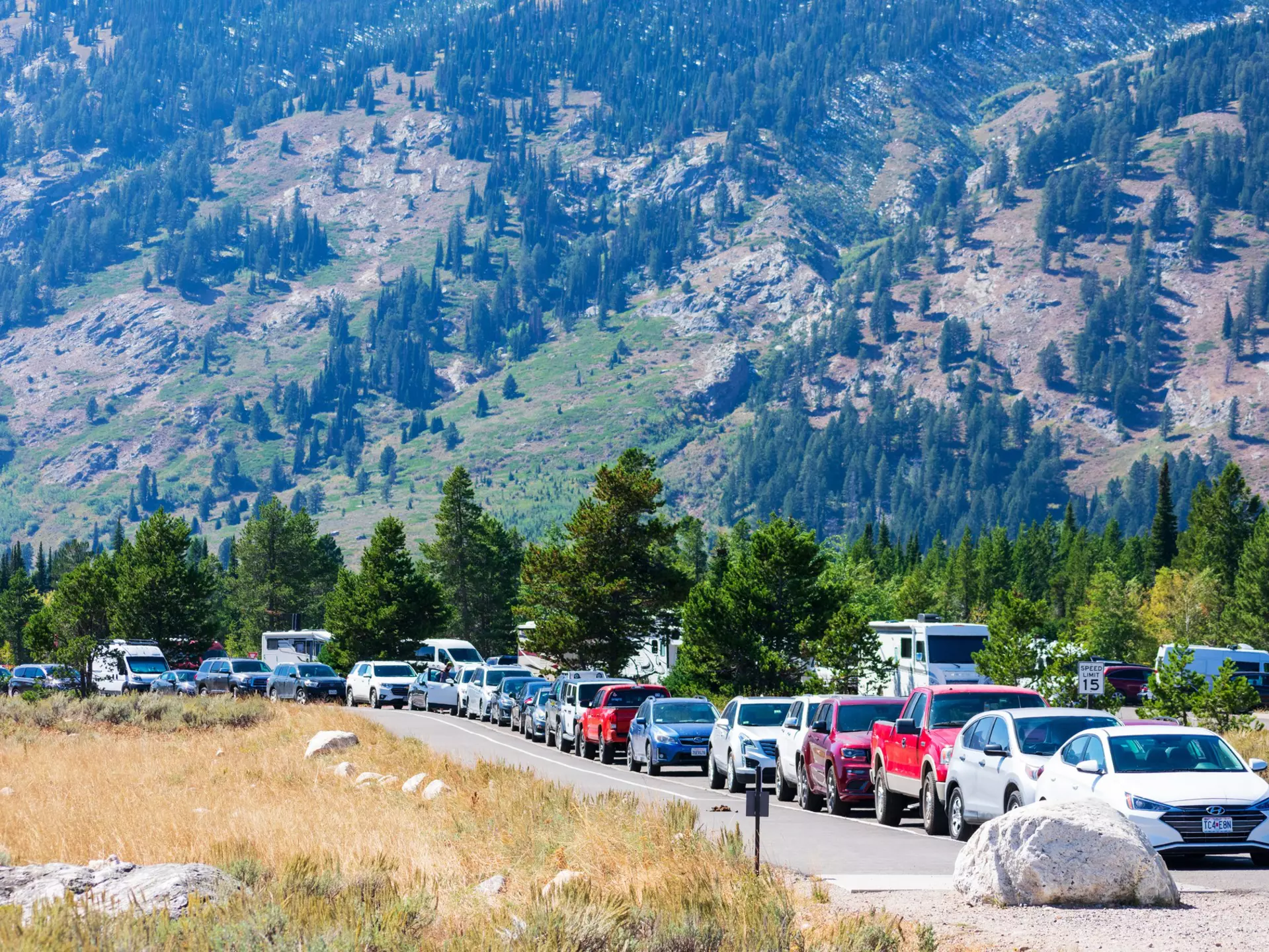 A large line of cars parked bumper to bumper on the road leading to Grand Teton National Park.