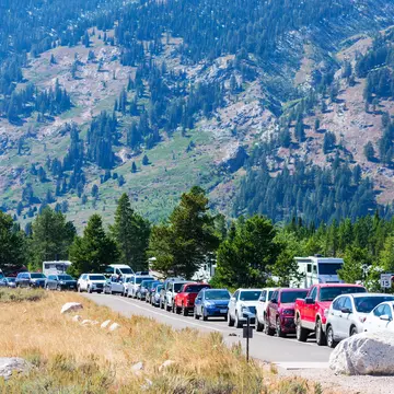 A large line of cars parked bumper to bumper on the road leading to Grand Teton National Park.