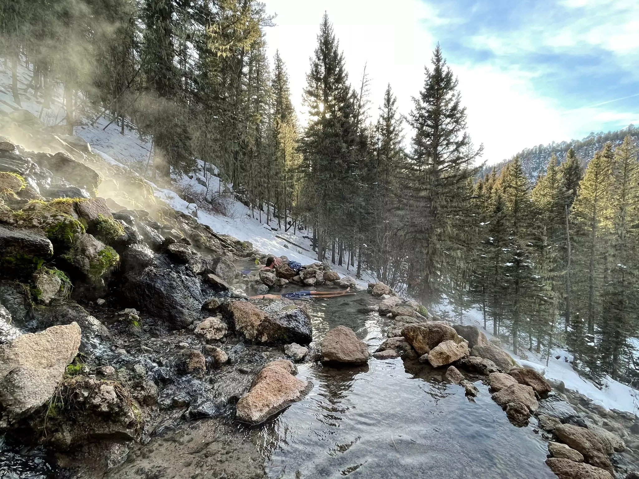 Steam rises from a hot spring deep in snow-covered forest.