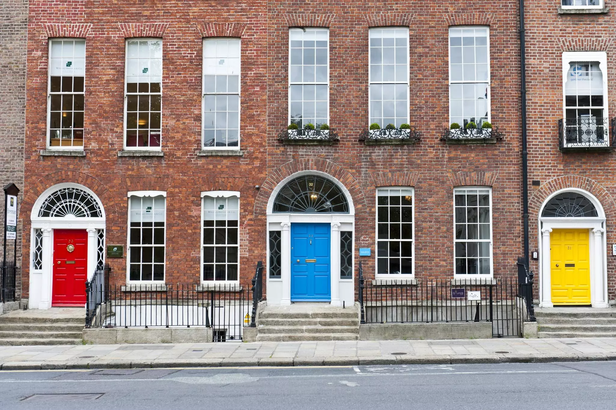 Three brick-fronted buildings are seen on a city street, one with a door painted red, one with a door painted blue and one with a door painted yellow.
