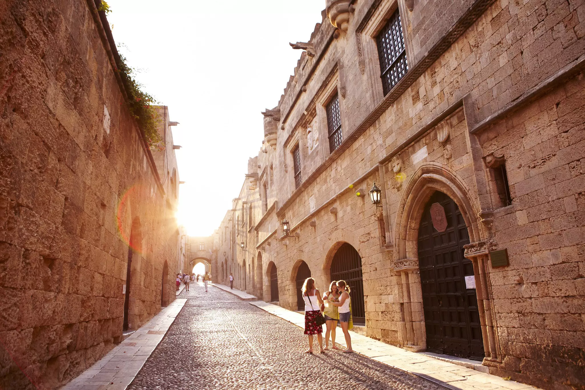 Women are seen on a cobbled street in a historic city, illuminated by rays of the setting sun.