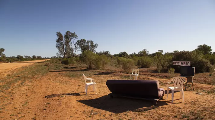 plastic chairs and an old couch sit in the desert with a painted sign that reads Rest Area