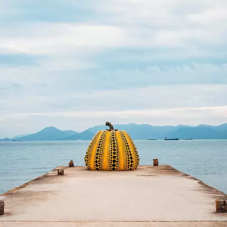 A yellow-and-black pumpkin art installation on a boardwalk in front of the sea. 