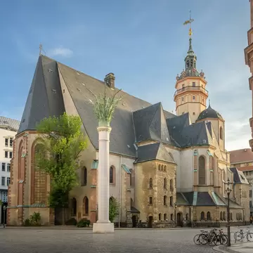 Leipzig's Nikolaikirche with steep slate roofs and ornate tower beside a white palm-topped column on a cobbled square