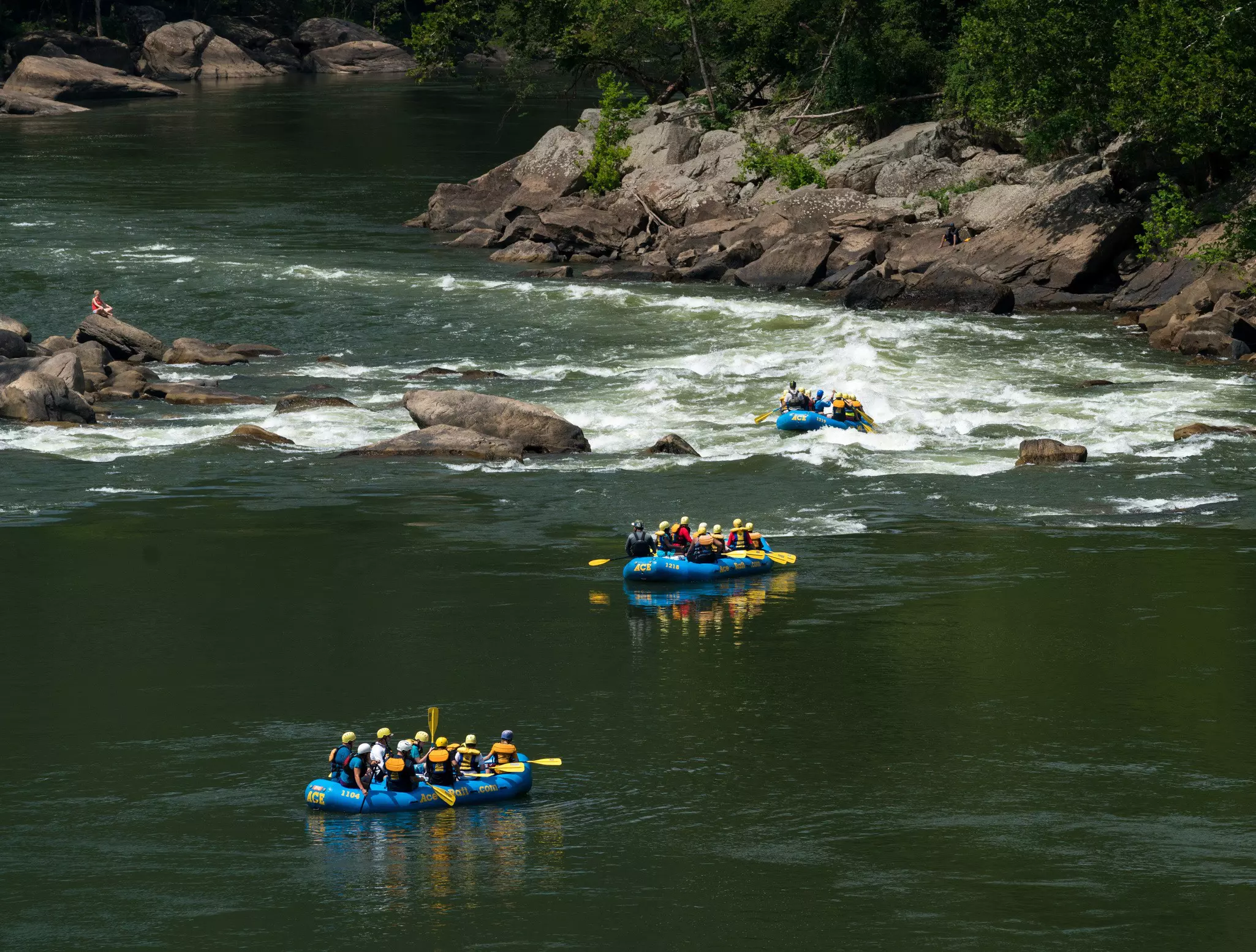 Three blue rafts filled with people approaching white water rapids.