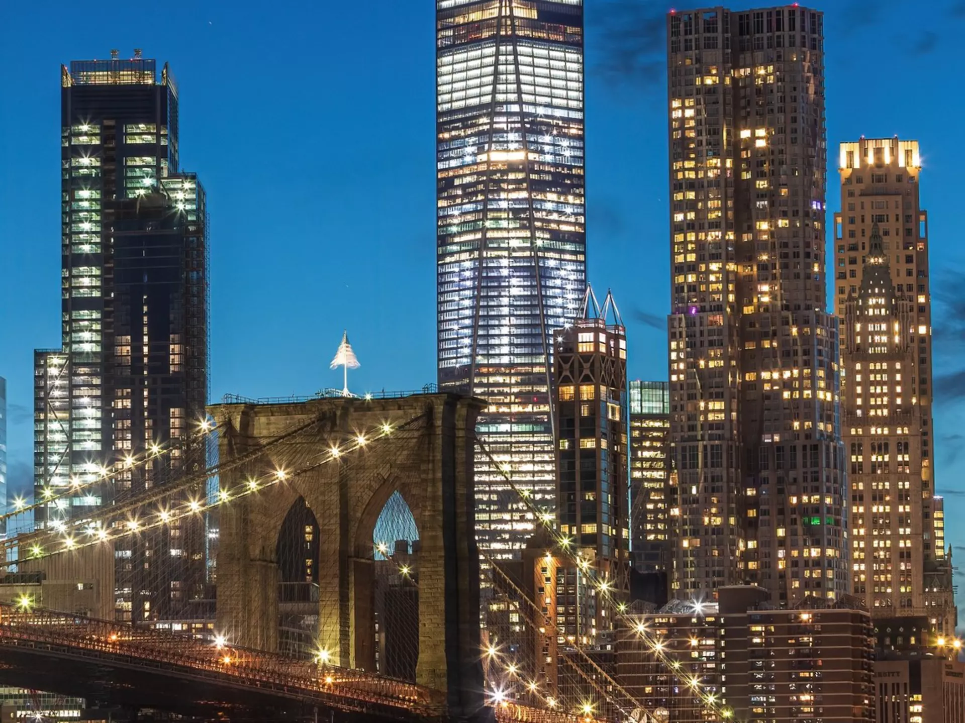 The photo captures the  Brooklyn Bridge at night from Brooklyn, with illuminated city lights reflecting on the calm water. The skyline, a modern skyscraper, and the serene park enhance the scene., License Type: media, Download Time: 2025-11-26T20:58:49.000Z, User: LP_YKhanna, Editorial: false, purchase_order: 65050 - Digital Destinations and Articles, job: LP, client: App Content, other: Yuvraj Khanna