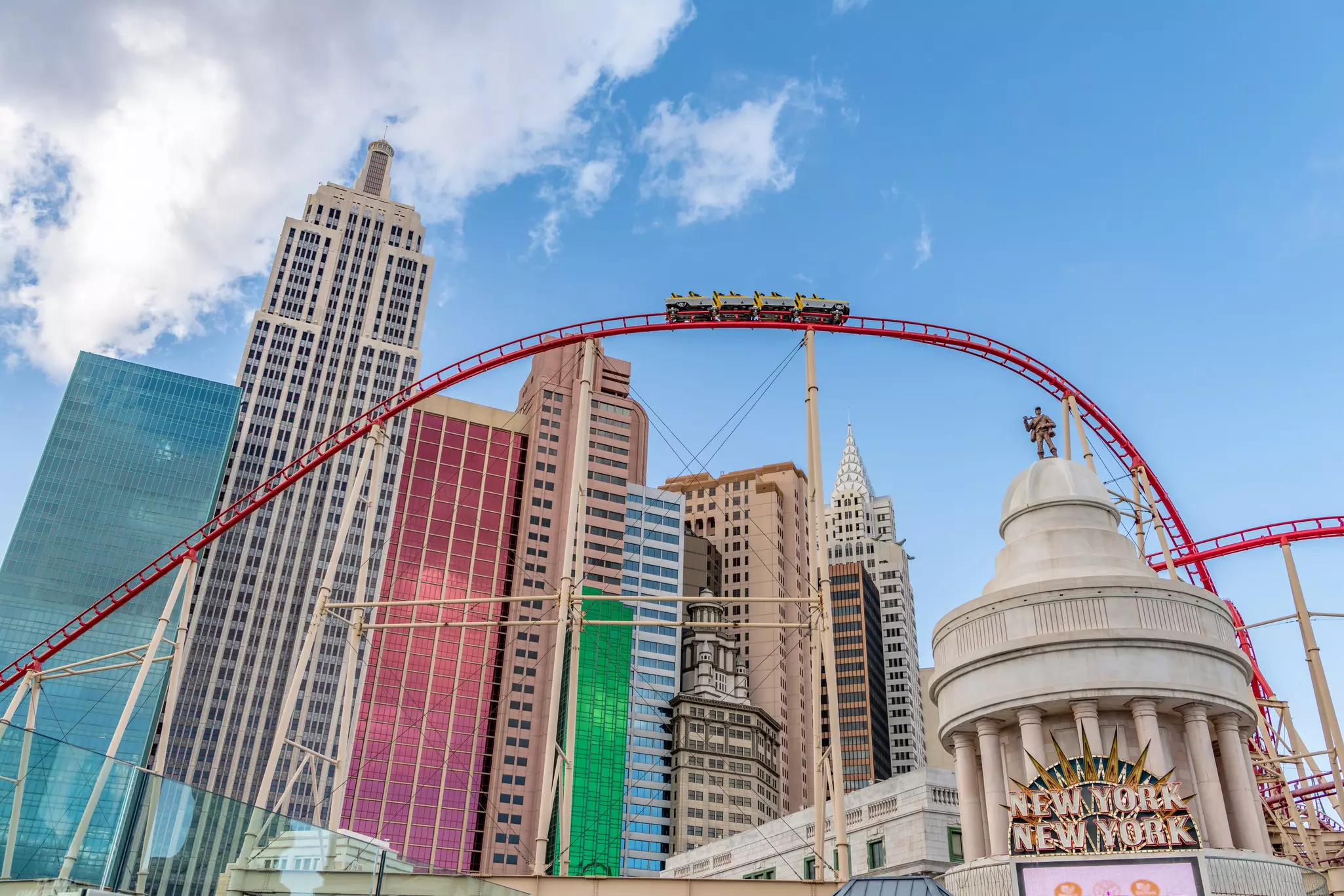 A roller coaster ascends just before a drop. The track surrounds a resort-hotel designed to look likt he skyline of a city.