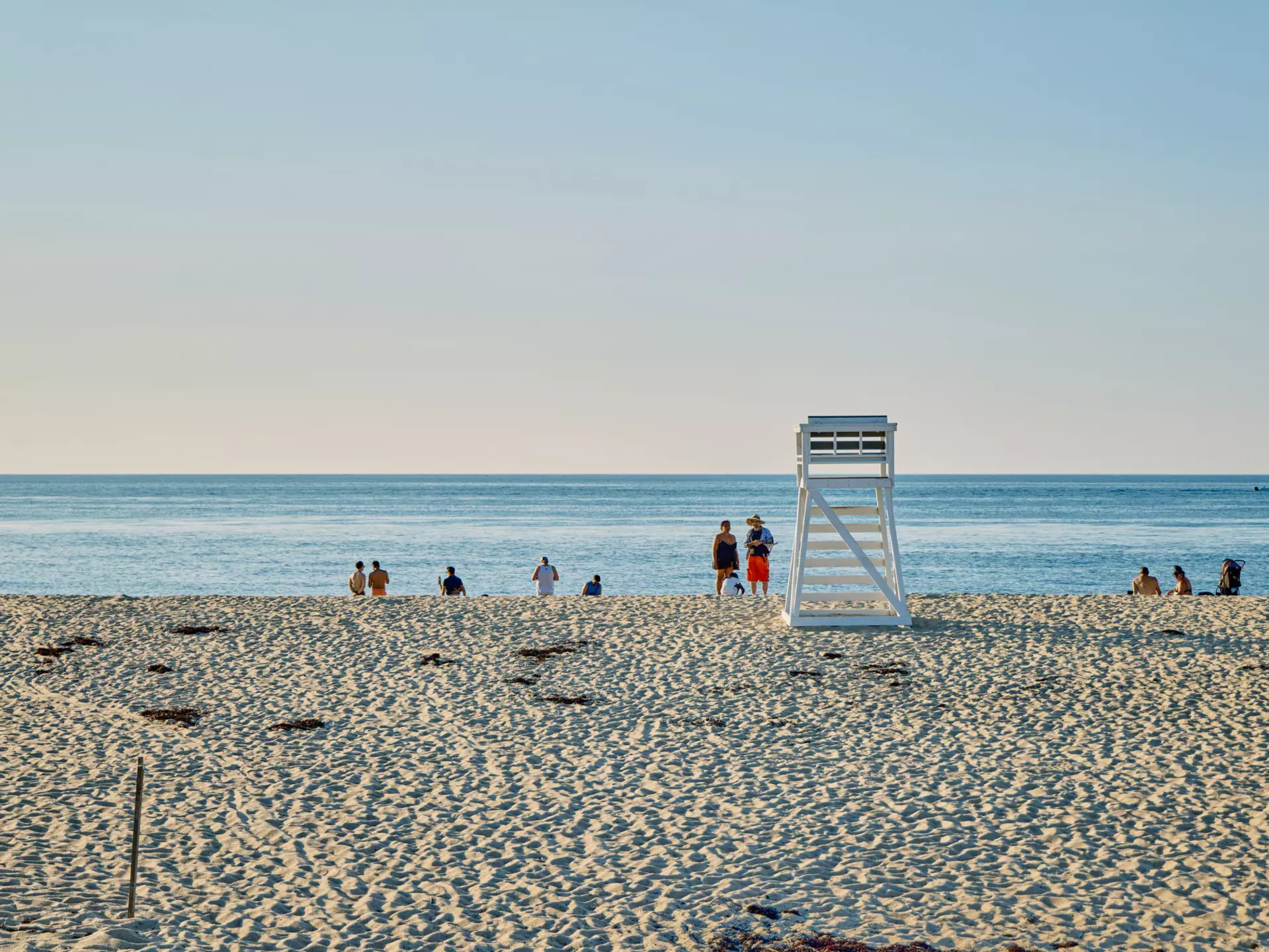 People on a sandy ocean beach with an empty lifeguard stand.