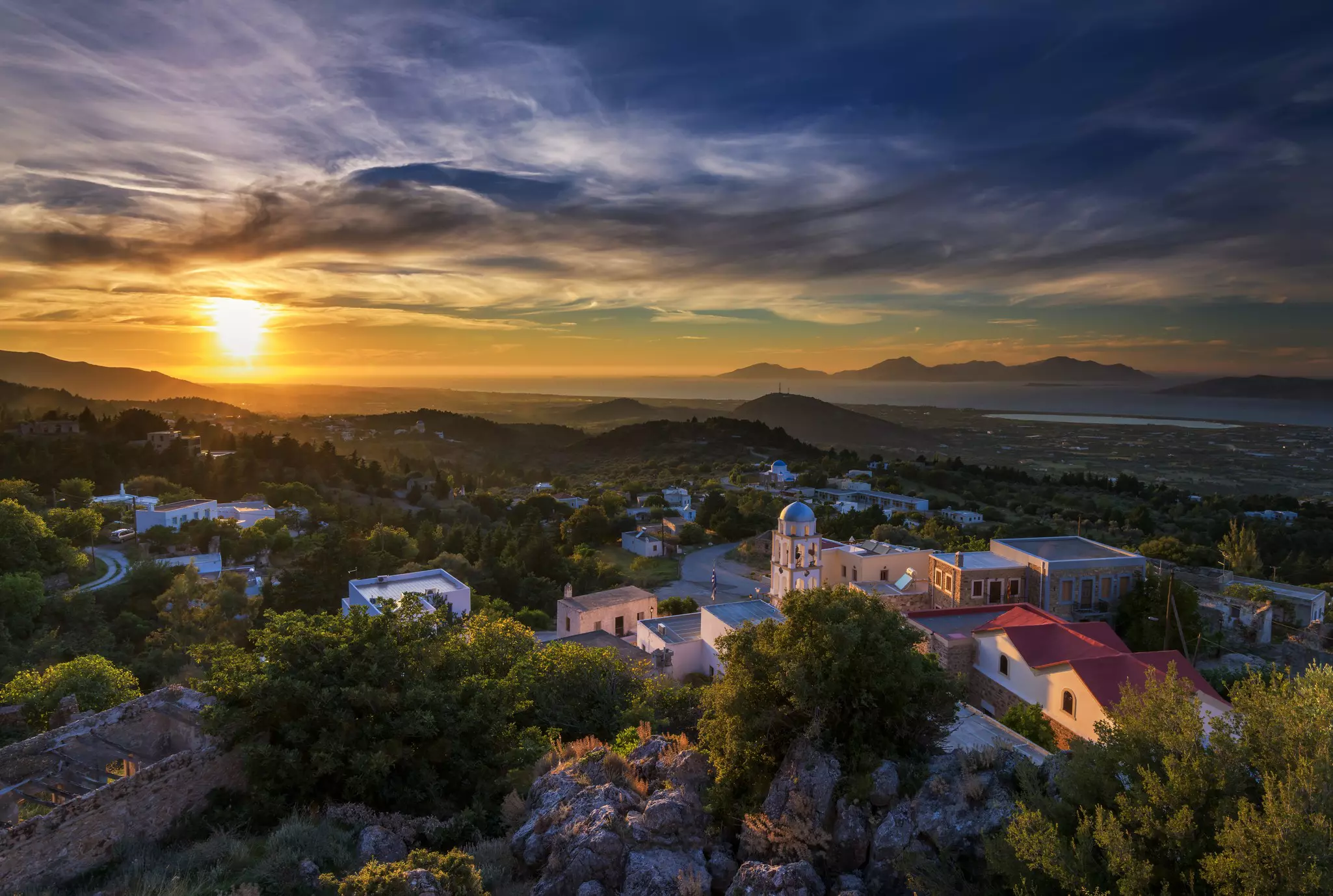 A wide view of a small mountain village lit by the setting sun. The sky shows dramatic sunset colors.