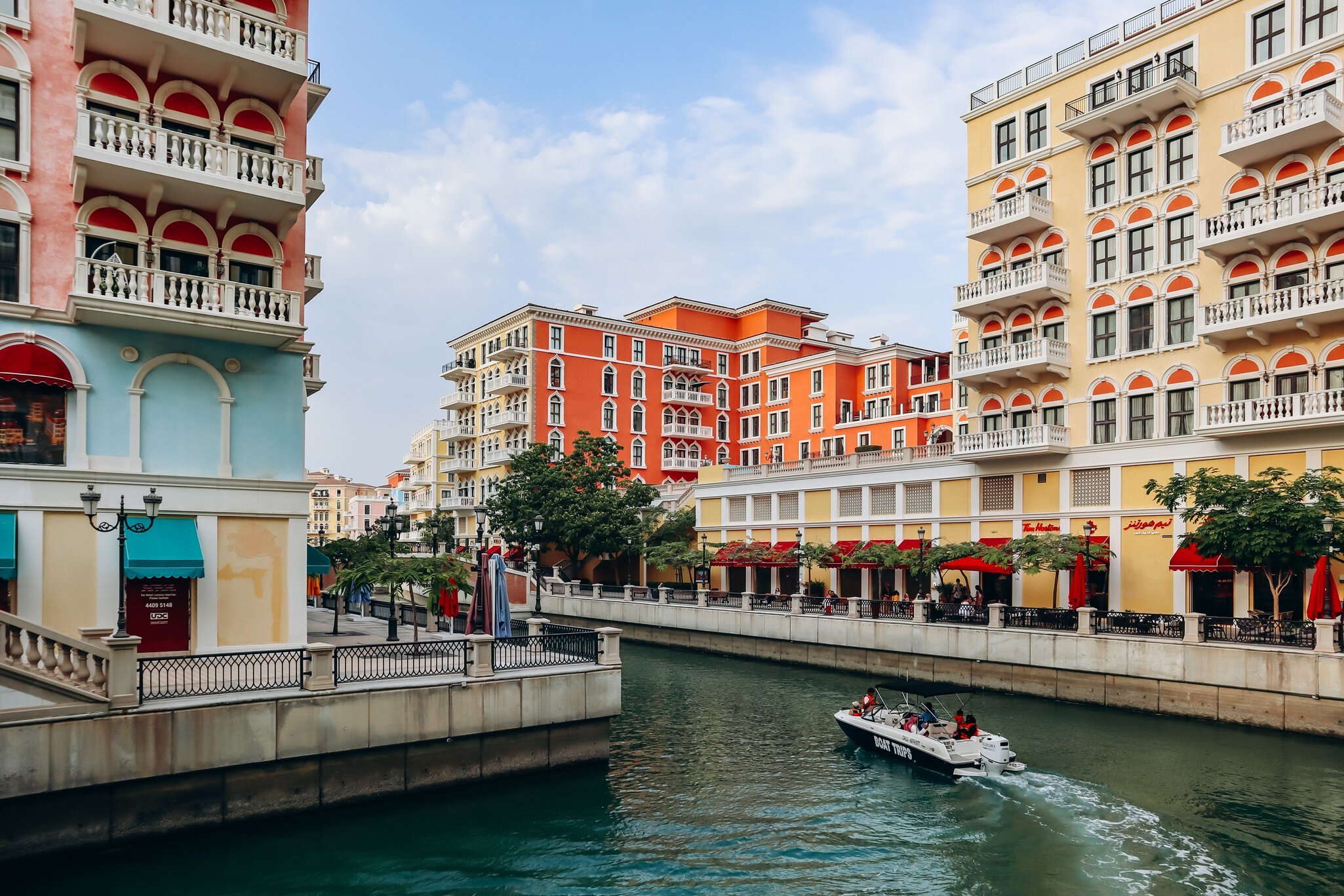 Boat cruises a canal between pastel Venetian-style blocks in Qanat Quartier on The Pearl, Doha; boat reads BOAT TRIPS