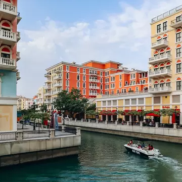 Boat cruises a canal between pastel Venetian-style blocks in Qanat Quartier on The Pearl, Doha; boat reads BOAT TRIPS