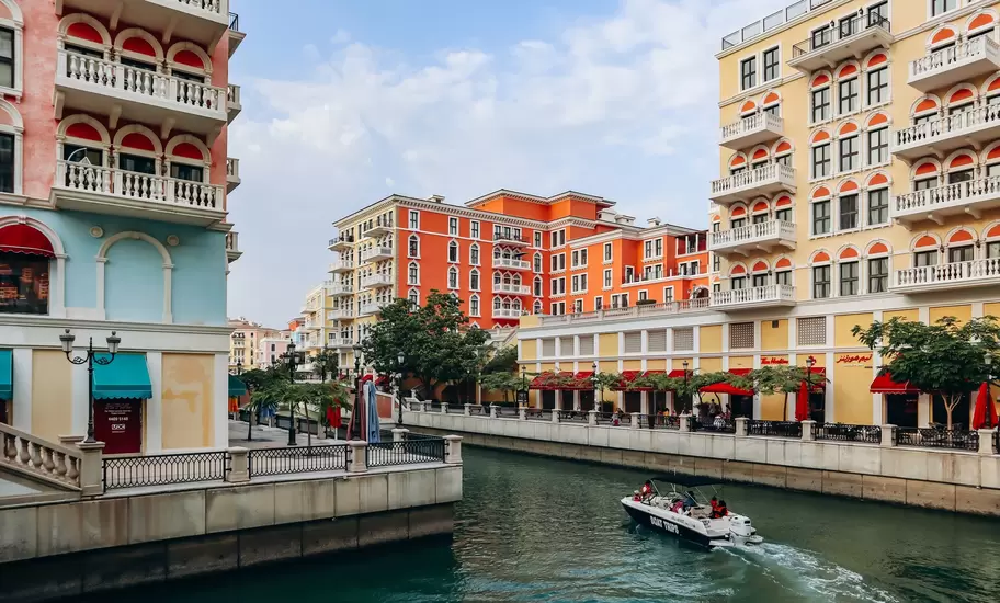 Boat cruises a canal between pastel Venetian-style blocks in Qanat Quartier on The Pearl, Doha; boat reads BOAT TRIPS