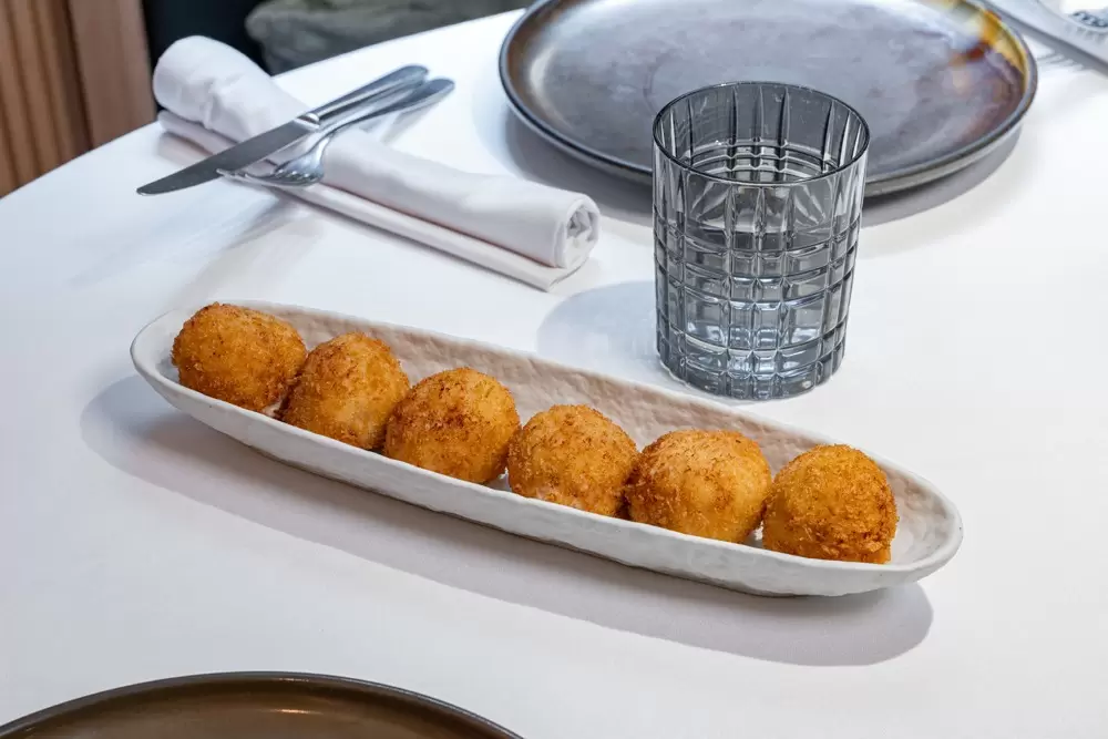 A narrow plate with six deep-friend round balls of croquetas at a restaurant in Spain.