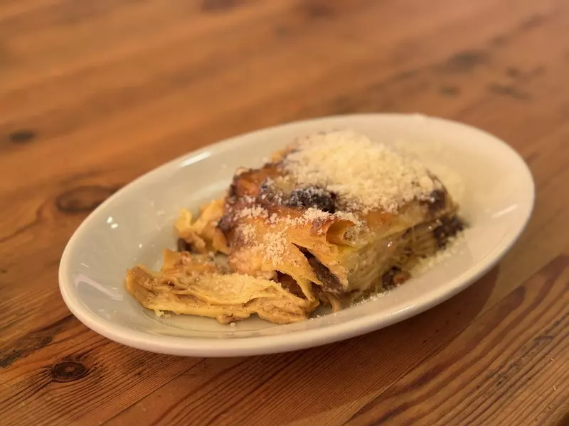 White plate with lasagna covered in parmesan cheese on a wooden table
