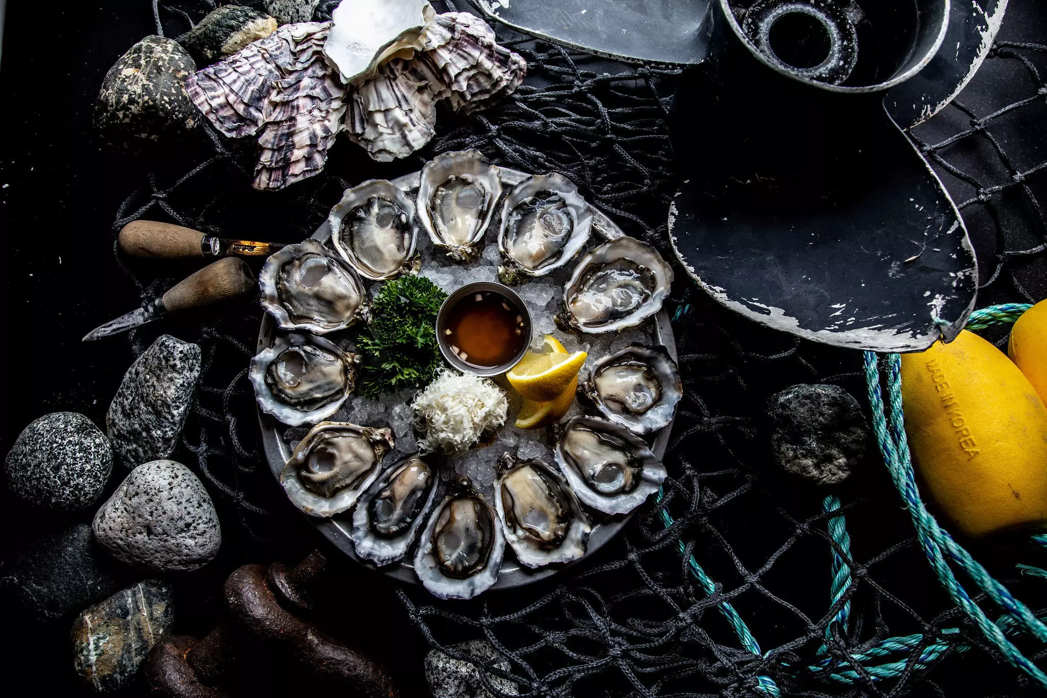 A round dish of oysters on a table. Lemon, oil and garnish sit in the center of the plate.