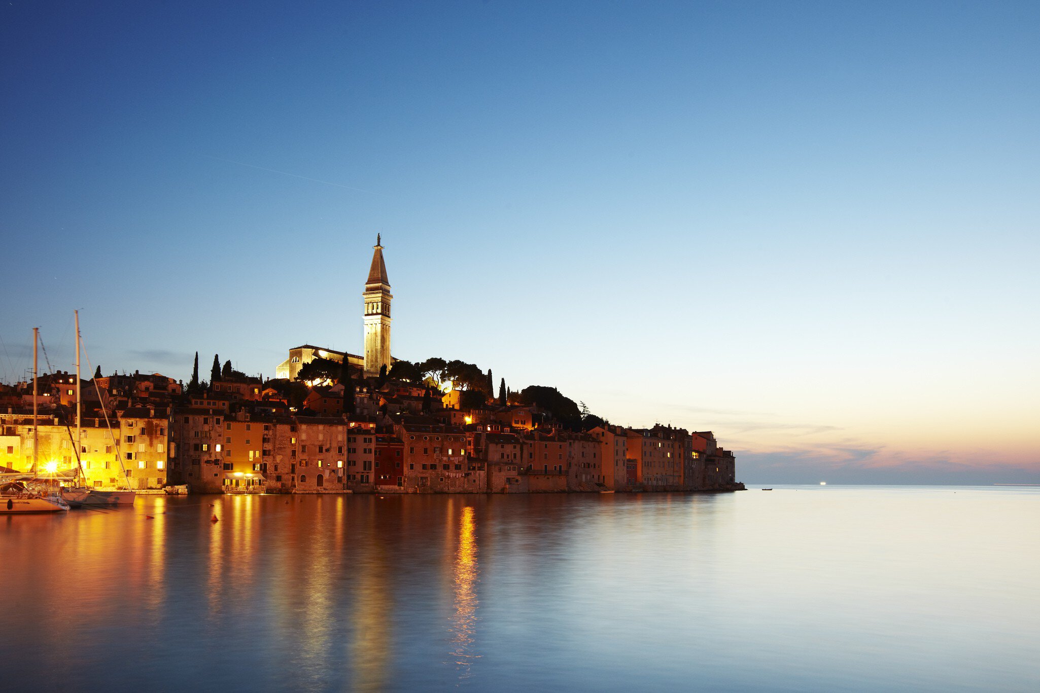View of port town and tower of Saint Euphemia's basilica at dusk.