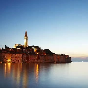View of port town and tower of Saint Euphemia's basilica at dusk.