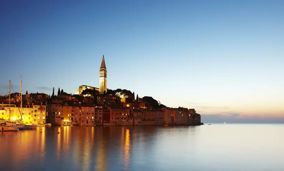 View of port town and tower of Saint Euphemia's basilica at dusk.