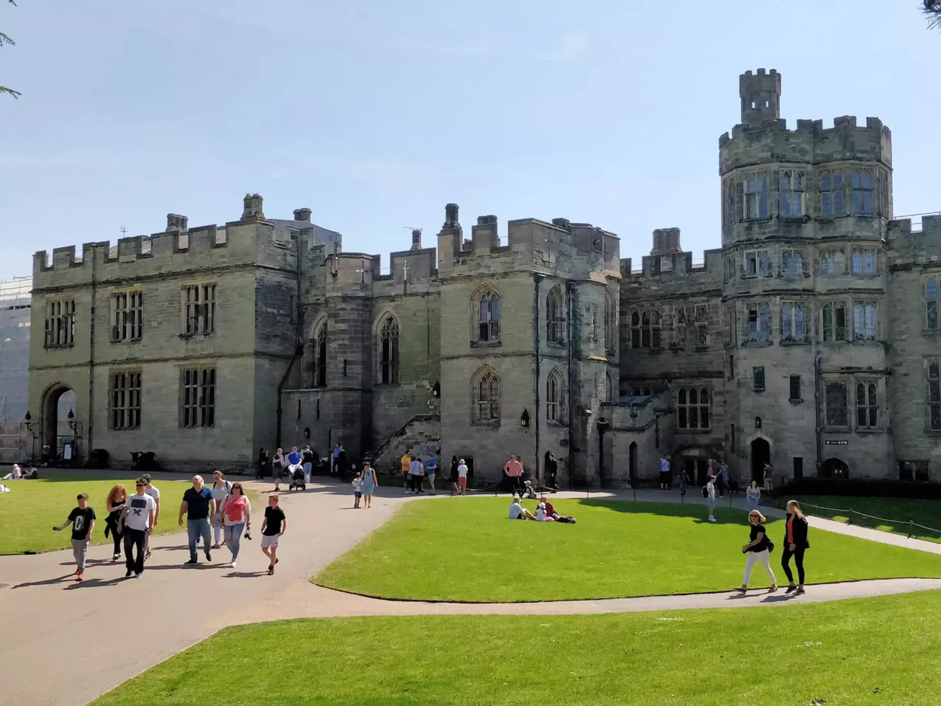 People explore the beautiful grounds of a large castle with turrets and huge stone battlements