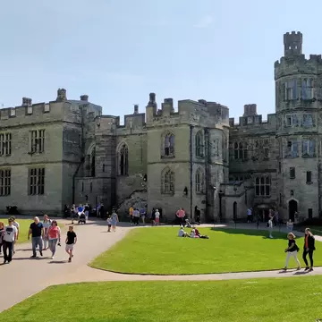 People explore the beautiful grounds of a large castle with turrets and huge stone battlements