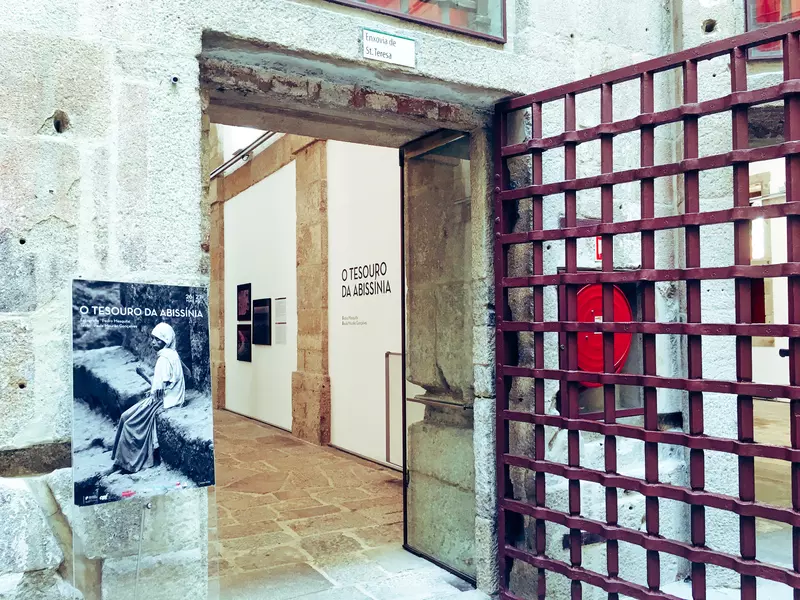 A red gate in a rough doorway is open to a photography exhibit.