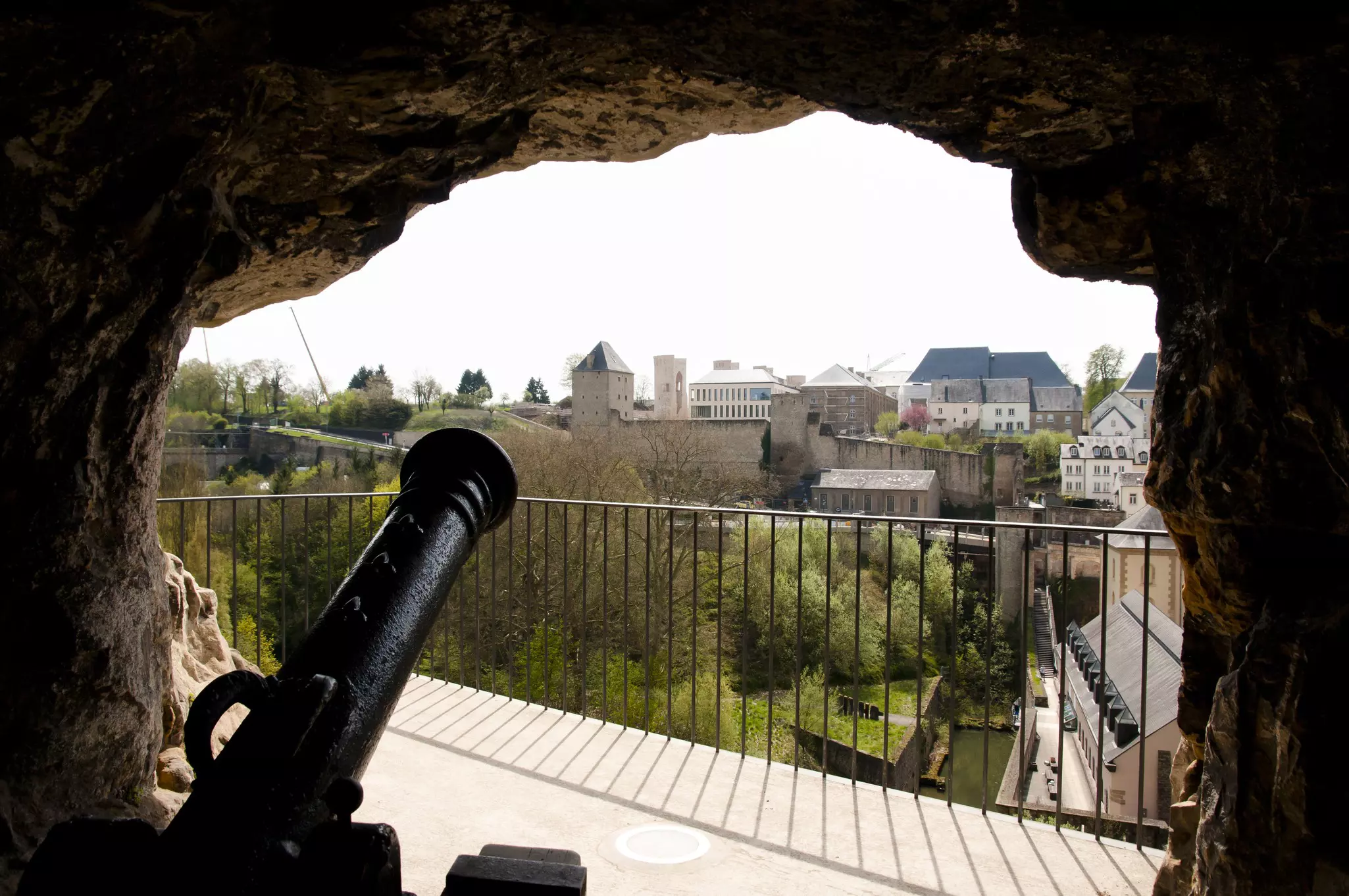 A cannon pokes out through an opening in a fortress in a city