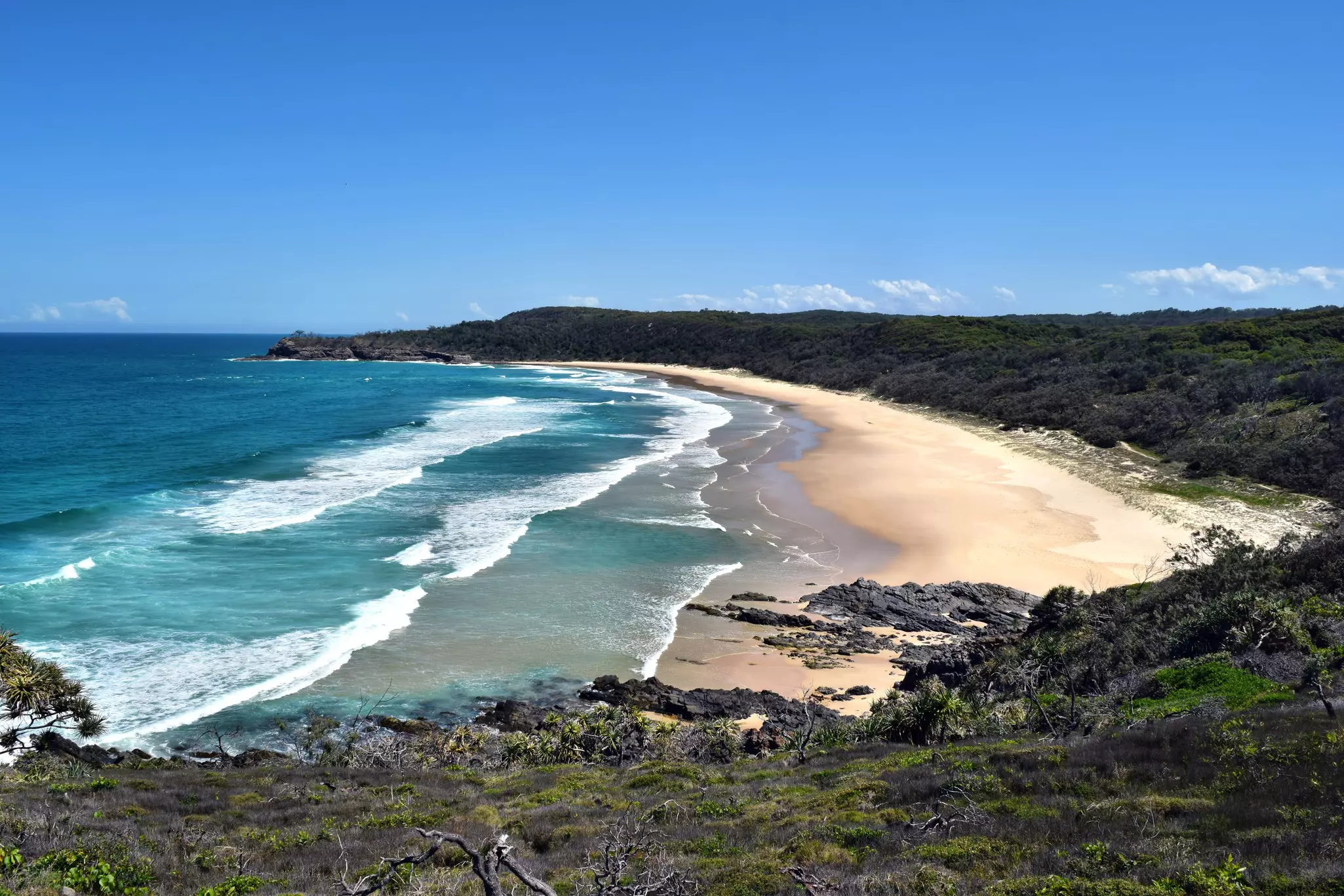 Aerial view of bay with sandy beach and ocean waves.