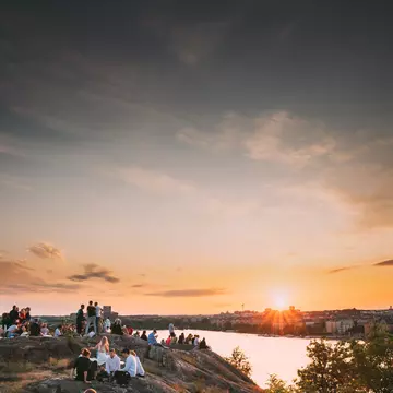Groups of people sat on a cliff top looking out over a city at sunset