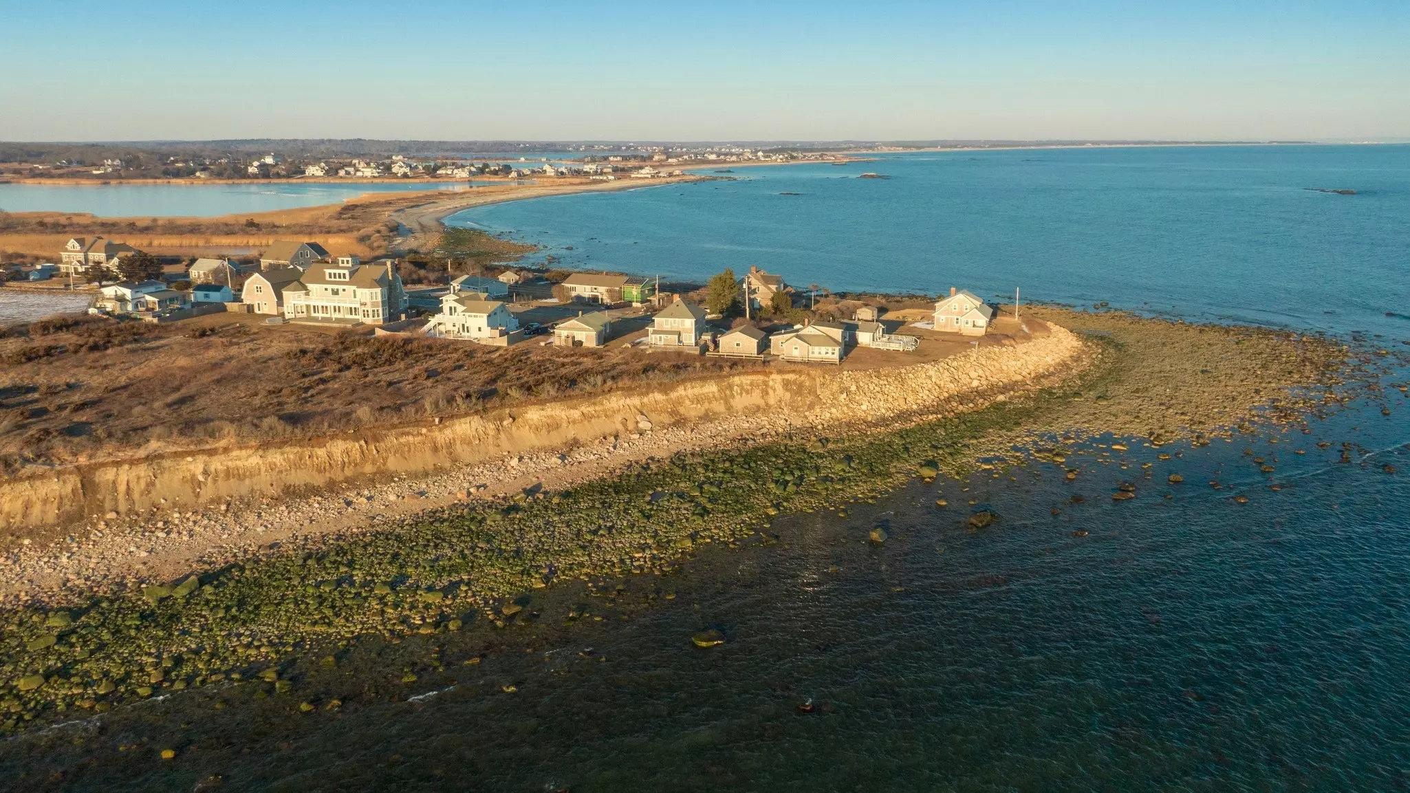 Homes along a pebbly shore near an isthmus by the sea.