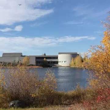 Concrete museum building with barrel roofs on the shore of Frame Lake, framed by yellow autumn birches in Yellowknife