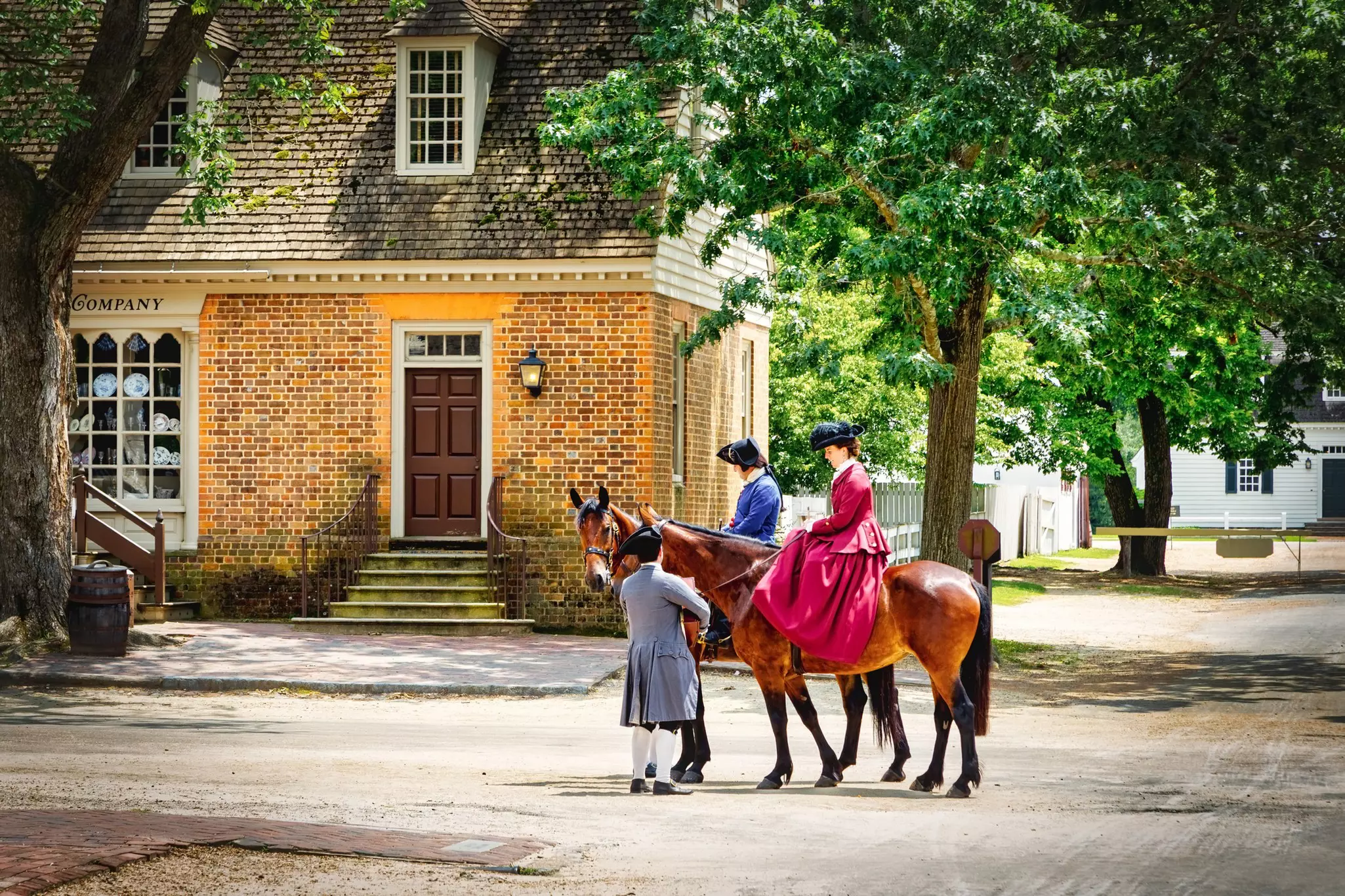 Three people in colonial dress, two on horseback, in a preserved historic town