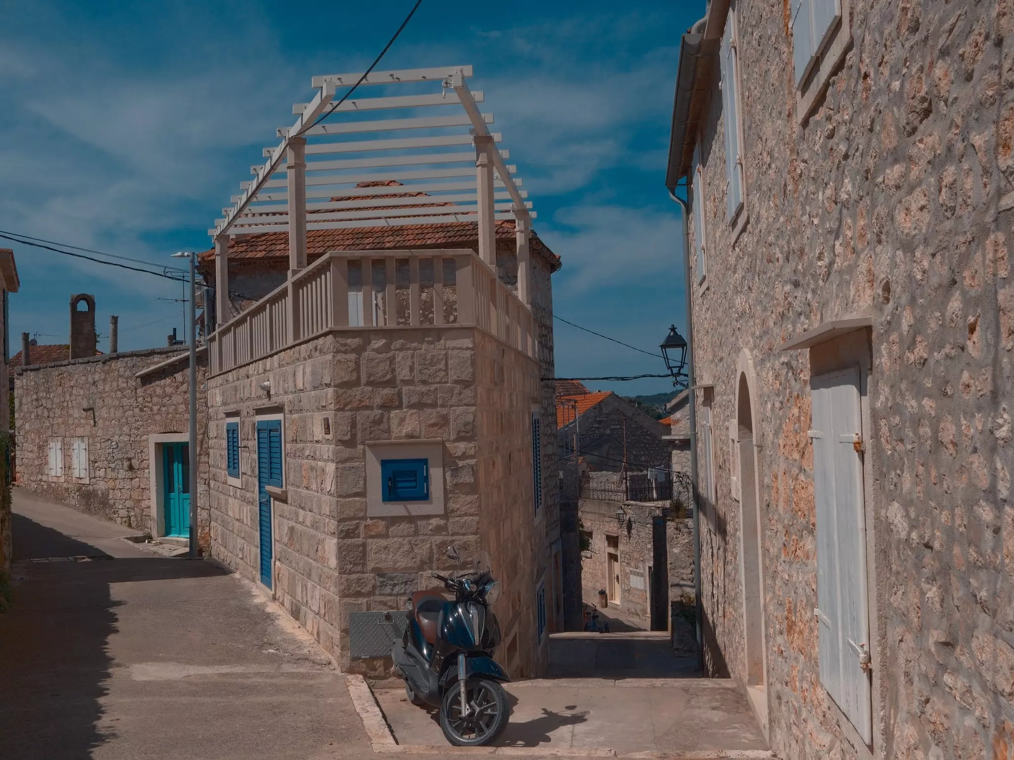 A motor scooter is parked in front of a tall stone house on a very narrow lane