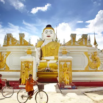 Novice monks cycling past 26-foot high sitting Buddha at Yan Aung Nan Aung Hsu Taung Pyi Pagoda near Inle Lake.