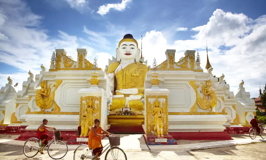 Novice monks cycling past 26-foot high sitting Buddha at Yan Aung Nan Aung Hsu Taung Pyi Pagoda near Inle Lake.