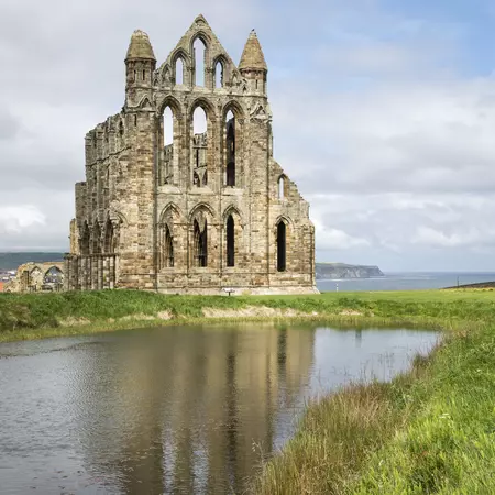 The ruins of Whitby Abbey in North Yorkshire, with water and fields in the foreground. 