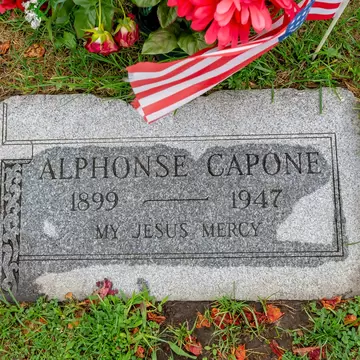 Granite grave marker inscribed Alphonse Capone 1899–1947 My Jesus Mercy, with a small US flag and red flowers