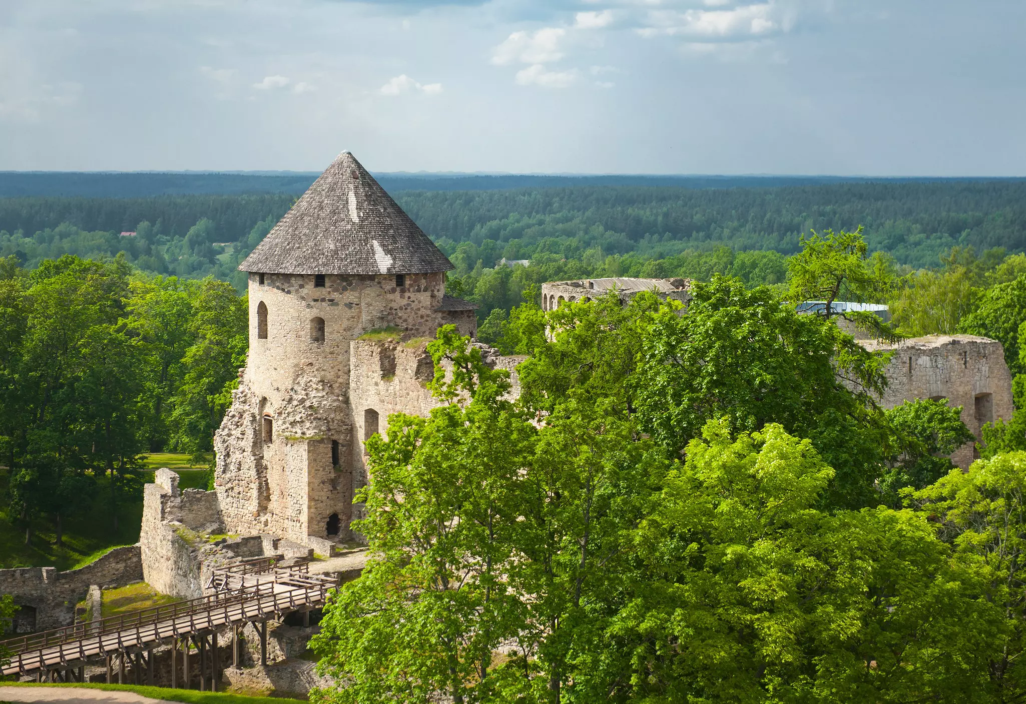 The fascinating ruins of Cēsis Castle, surrounded by foliage on all sides. a bridge extends from the castle to the left.