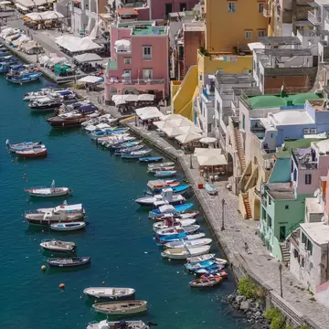 Marina di Corricella on Procida from above, with small boats moored in green water below pink, yellow and white houses.