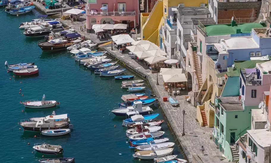 Marina di Corricella on Procida from above, with small boats moored in green water below pink, yellow and white houses.