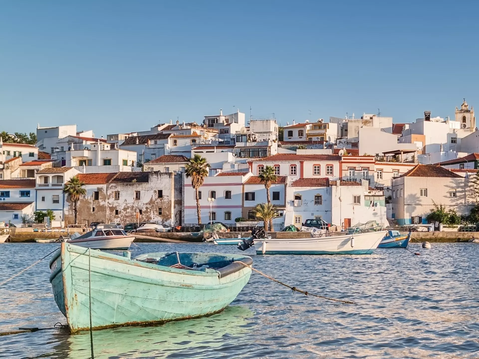 Small fishing boats moored in a harbor near a small seaside town of white buildings with red roofs.